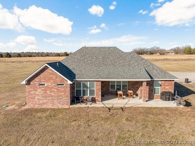 rear view of property featuring a yard, a shingled roof, brick siding, and a patio