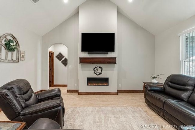 living room with high vaulted ceiling, a lit fireplace, arched walkways, and baseboards