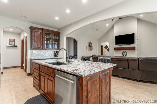 kitchen with a sink, a center island with sink, arched walkways, and stainless steel dishwasher