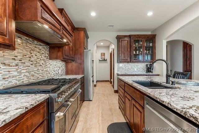 kitchen featuring visible vents, arched walkways, stainless steel appliances, premium range hood, and a sink