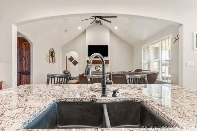 kitchen with arched walkways, light stone counters, a sink, open floor plan, and vaulted ceiling