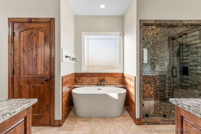 bathroom with a stall shower, vanity, a freestanding bath, and wainscoting