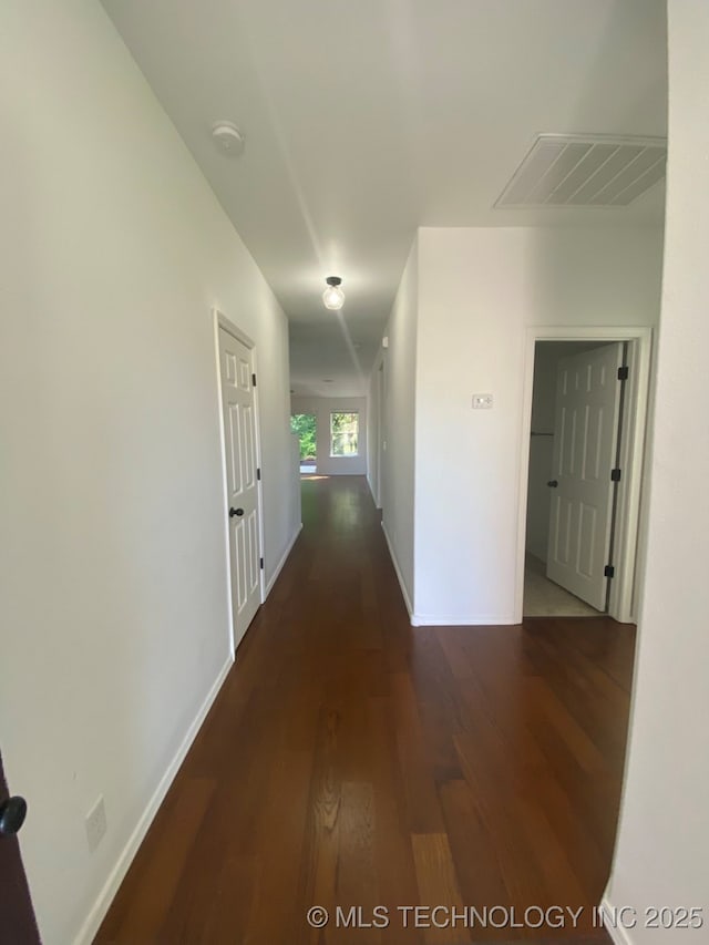 hallway with wood finished floors, visible vents, and baseboards