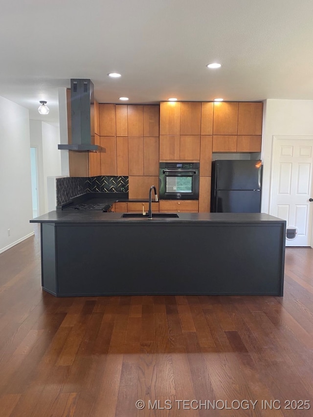 kitchen featuring a sink, wall chimney range hood, brown cabinets, black appliances, and dark countertops