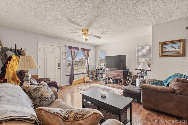 living room featuring a textured wall, ceiling fan, a textured ceiling, and wood finished floors