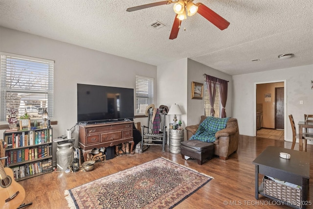 living room featuring a ceiling fan, visible vents, a textured ceiling, and wood finished floors