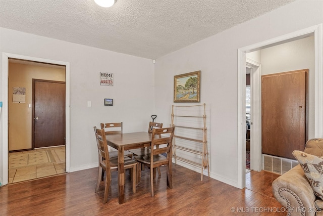 dining area featuring baseboards, a textured ceiling, visible vents, and wood finished floors