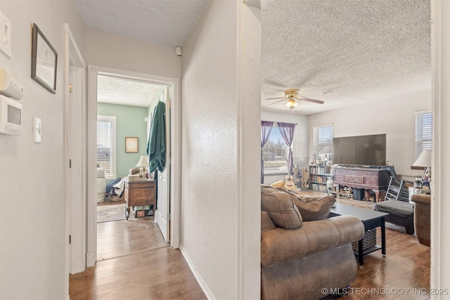 living room with a textured ceiling, a textured wall, ceiling fan, and wood finished floors