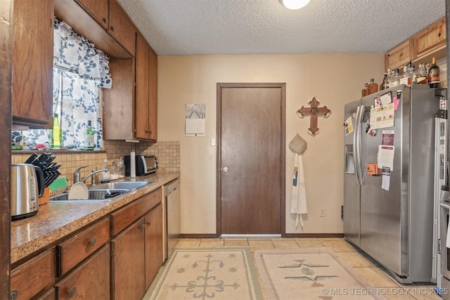 kitchen featuring a textured ceiling, a sink, light countertops, appliances with stainless steel finishes, and tasteful backsplash