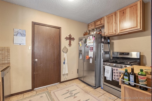 kitchen with stainless steel appliances, a textured ceiling, baseboards, and light tile patterned floors