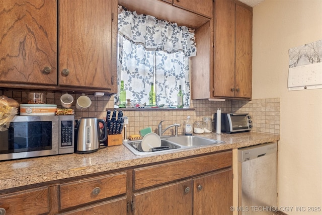 kitchen featuring brown cabinets, light countertops, decorative backsplash, appliances with stainless steel finishes, and a sink