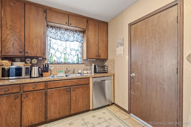 kitchen with appliances with stainless steel finishes, brown cabinets, a sink, and tasteful backsplash