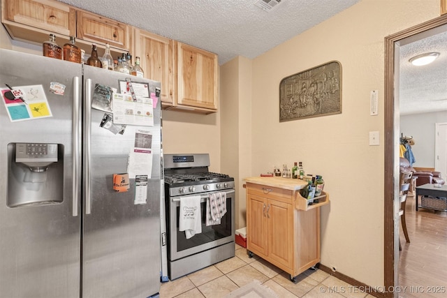 kitchen with stainless steel appliances, light tile patterned floors, a textured ceiling, and light brown cabinetry