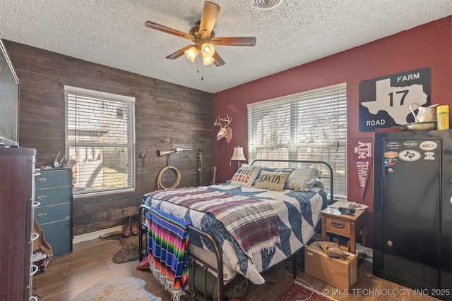 bedroom featuring wood walls, multiple windows, wood finished floors, and a textured ceiling