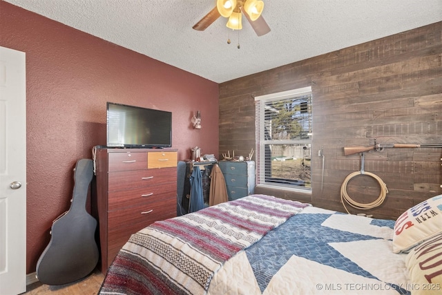 bedroom featuring a ceiling fan, a textured wall, wooden walls, and a textured ceiling