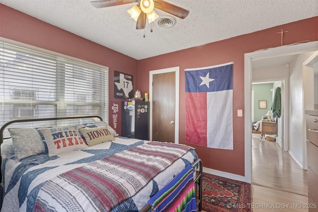 bedroom featuring visible vents, baseboards, ceiling fan, wood finished floors, and a textured ceiling