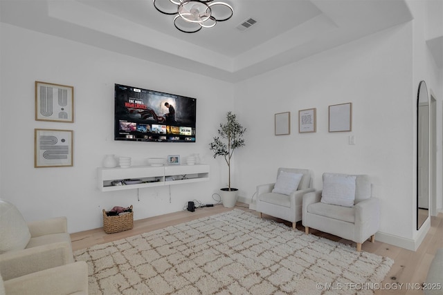 living area featuring baseboards, visible vents, a raised ceiling, and wood finished floors