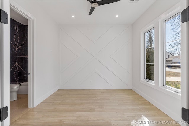 spare room featuring light wood finished floors, baseboards, and a decorative wall