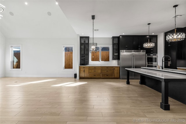 kitchen featuring light wood-style flooring, stainless steel appliances, light countertops, dark cabinetry, and decorative backsplash