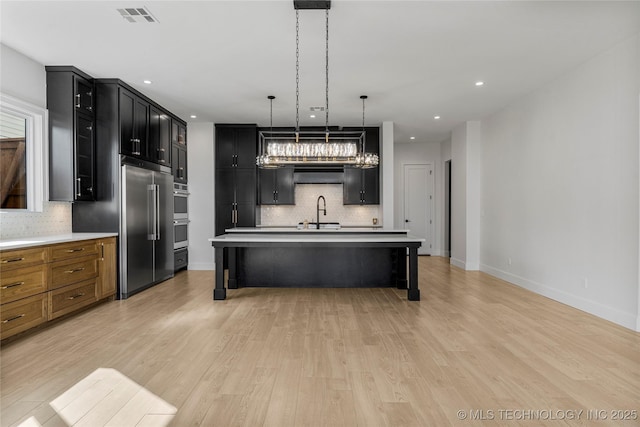 kitchen featuring visible vents, light wood-style flooring, a breakfast bar area, and dark cabinetry