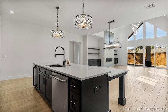 kitchen with visible vents, open floor plan, dark cabinetry, light wood-type flooring, and a sink