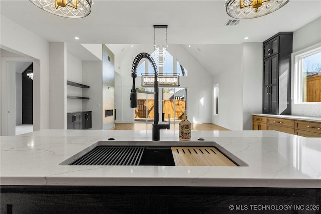 kitchen featuring a sink, light stone counters, a chandelier, and dark cabinetry