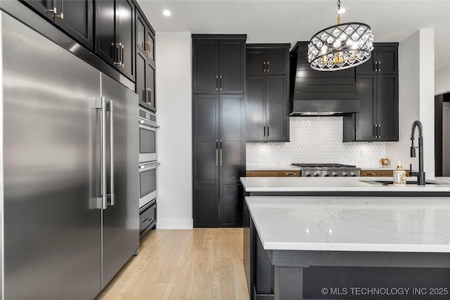 kitchen featuring wall chimney range hood, stainless steel appliances, and dark cabinetry