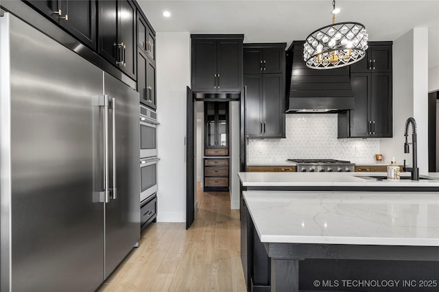 kitchen featuring tasteful backsplash, appliances with stainless steel finishes, a sink, light wood-type flooring, and dark cabinetry