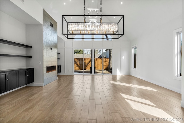 unfurnished living room featuring light wood-style floors, visible vents, a fireplace, and a high ceiling