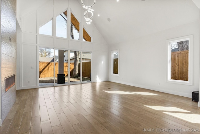 unfurnished living room featuring high vaulted ceiling, wood finished floors, a tile fireplace, and baseboards