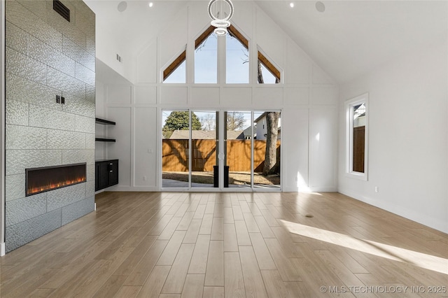 unfurnished living room with high vaulted ceiling, wood finished floors, visible vents, baseboards, and a tiled fireplace