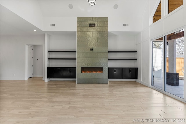 unfurnished living room featuring light wood finished floors, built in shelves, visible vents, and a tiled fireplace