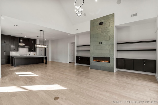 unfurnished living room featuring baseboards, visible vents, a tile fireplace, light wood-style floors, and high vaulted ceiling