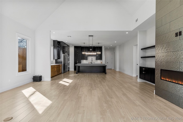 unfurnished living room featuring light wood-style floors, a tile fireplace, visible vents, and high vaulted ceiling