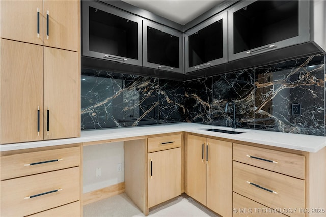 kitchen featuring a sink, backsplash, light brown cabinets, and glass insert cabinets