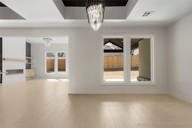 unfurnished room with a chandelier, plenty of natural light, a glass covered fireplace, and visible vents