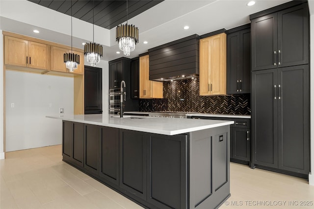 kitchen with decorative light fixtures, light countertops, wall chimney range hood, and an island with sink