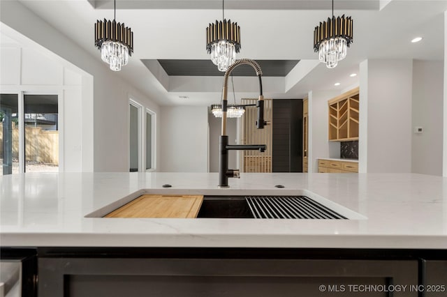 kitchen with a raised ceiling, light stone countertops, pendant lighting, a notable chandelier, and recessed lighting