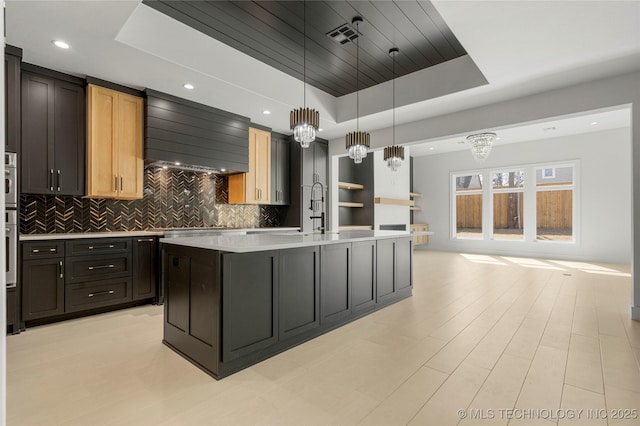 kitchen featuring tasteful backsplash, a raised ceiling, light countertops, visible vents, and premium range hood