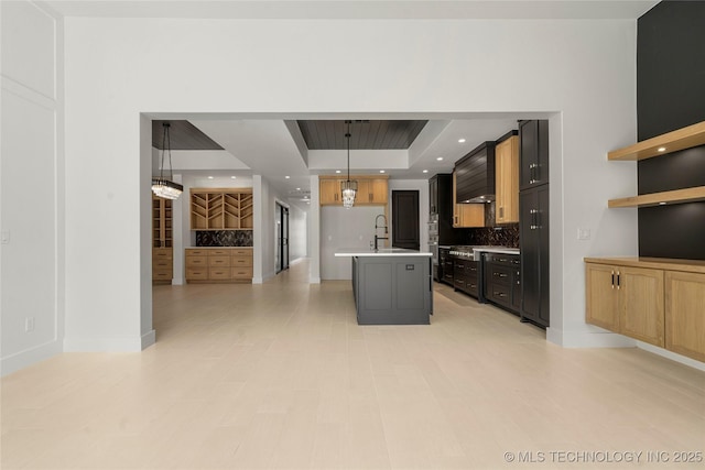 kitchen featuring a center island with sink, decorative backsplash, a raised ceiling, light countertops, and a sink