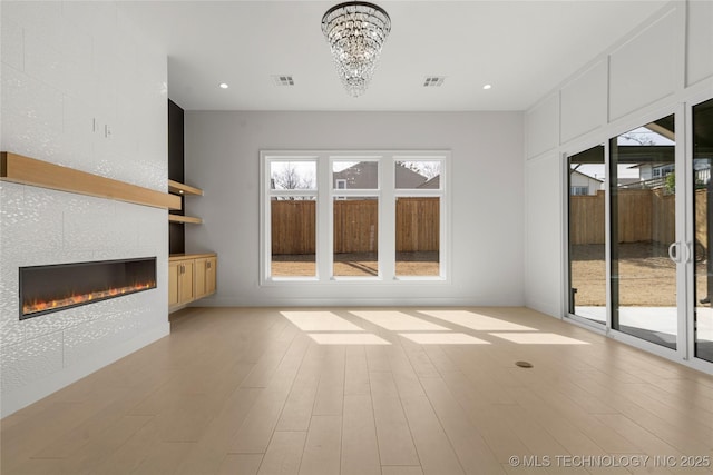 unfurnished living room featuring a tile fireplace, visible vents, and light wood-style floors