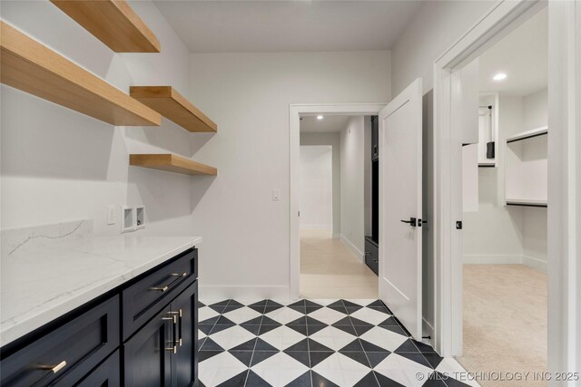 interior space featuring dark cabinetry, baseboards, open shelves, and light stone counters