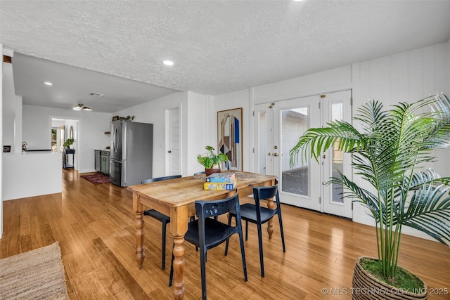 dining room with light wood finished floors, plenty of natural light, french doors, and a textured ceiling