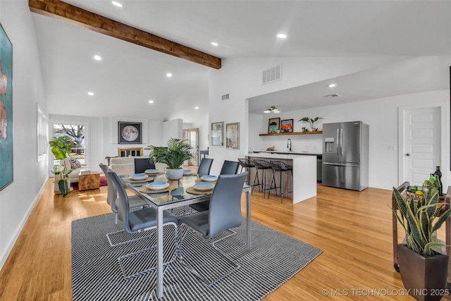 dining area with light wood-style flooring, beamed ceiling, visible vents, and high vaulted ceiling