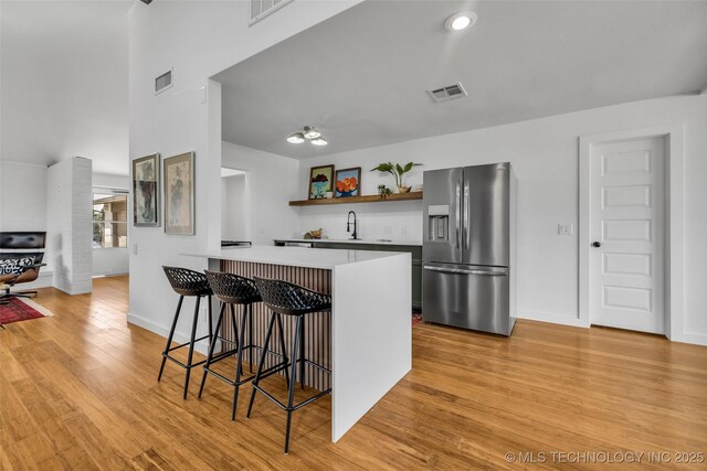 kitchen with visible vents, open shelves, a breakfast bar area, stainless steel fridge with ice dispenser, and light wood finished floors