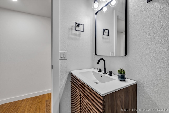 bathroom with a textured wall, vanity, baseboards, and wood finished floors