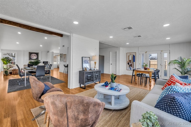 living room with lofted ceiling with beams, visible vents, a textured ceiling, and wood finished floors