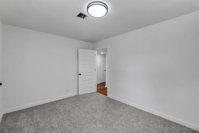 empty room featuring carpet flooring, visible vents, baseboards, and a textured ceiling