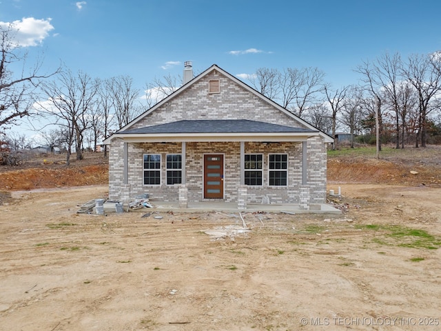 view of front of house with brick siding, a porch, and a chimney