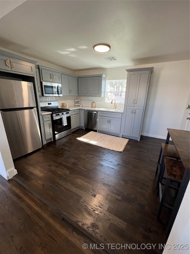 kitchen featuring dark wood-style floors, gray cabinets, stainless steel appliances, and a sink